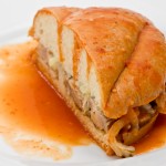 Mexican Torta Ahogada, or drowned sandwich with pork on a white plate.